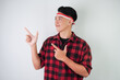 © Rizky - Excited amazed young asian man wearing Indonesian flag headband and pointing fingers on copy space beside, isolated over white background. Concept for Indonesian Independence Day.