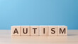 © hardvicore - Wooden cubes with word AUTISM on wooden table against light blue background.