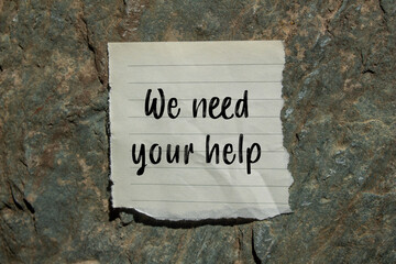 We need your help message written on ripped torn paper piece on stone background. Conceptual we need your help symbol. Copy space.