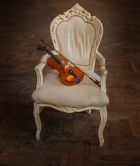 wooden violin lies on armchair old vintage style, classic furniture royal throne chair white fabric upholstery dark gothic fantasy room background. Musical instrument without people filming object 4k