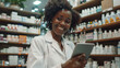© VK Studio - A cheerful pharmacist holds a tablet in a well-stocked pharmacy, surrounded by shelves filled with various medications.