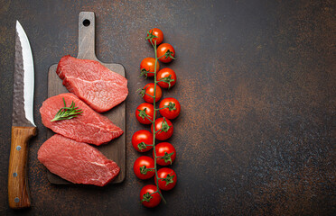 Three raw uncooked meat beef top sirloin steaks on wooden cutting board with rosemary on wooden cutting board with cherry tomatoes branch, knife on dark rustic background top view. Copy space