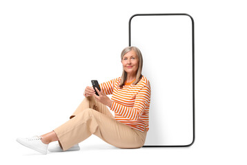 Poster - Happy mature woman holding mobile phone and sitting near big smartphone on white background