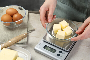 Wall Mural - Woman weighing butter on kitchen scale at grey table, closeup