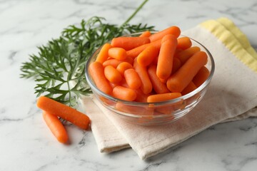 Wall Mural - Baby carrots in bowl and green leaves on white marble table