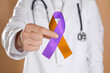 © New Africa - World Psoriasis Day. Doctor with orange and orchid ribbon as symbol of support on dark beige background, closeup