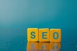 © CozyDigital - SEO. Yellow wooden cubes with the word SEO on them. Blue background. Search engine optimization