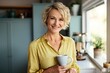 © gankevstock - Cheerful mature blonde woman holding cup in cozy kitchen