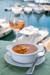 Homemade tasty fish or bisque soup with croutons served with glass of cold rose wine and view on yacht boats and houses of Port Grimaud, French Riviera, France. Food of Provence