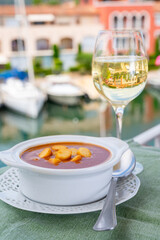 Homemade tasty fish or bisque soup with croutons served with glass of cold white wine and view on yacht boats and houses of Port Grimaud, French Riviera, France. Food of Provence