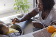 © Anna Berkut/Stocksy - mother feeding baby child in high chair at home