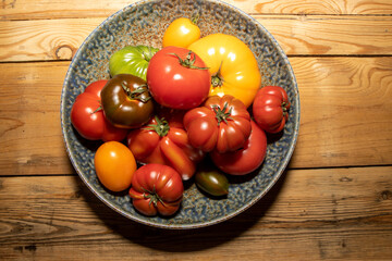 A bowl of different size and colour tomatoes on a wooden kitchen table