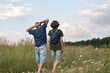 © Viktoriia - Family hiking in countryside, father and his teenage son walking in meadow with beautiful flowers, blue sky with clouds in summer day