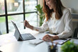 © PaeGAG - Businesswoman Working on Laptop in Modern Office with Natural Light and Greenery in the Background