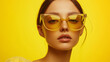 © Natali - Close-up portrait of a woman wearing stylish yellow-tinted sunglasses against a bright yellow background. Ideal for fashion editorials, summer campaigns, and eyewear advertisements