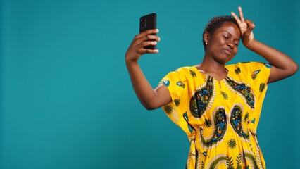 Wall Mural - Female model being excited and happy on her pictures in studio, taking photos with confidence and good vibes with her smartphone. Young woman photographing herself for portraits. Camera B.