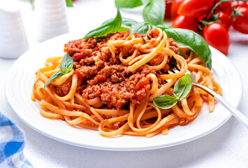 Wall Mural - Prepared spaghetti in bolognese sauce or pasta with minced meat and tomatoes decorated green basil, white table background, top view