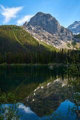 Wall Mural - Incredibly beautiful transparent, emerald calm lake with reflection of rocky mountain on the Black Prince Cirque Trail. Majestic Canadian mountains with snow on sunny summer day in Alberta, Kananaskis