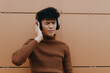 © SHOTPRIME STUDIO - Stylish young asian man wearing headphones standing in front of a brown wall