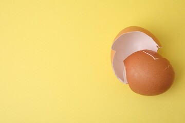 Wall Mural - Pieces of broken eggshells on yellow background, top view. Space for text