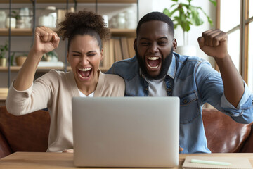 Overjoyed African American couple cheering and celebrating a win in front of a laptop at home