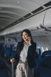 © ARMMY PICCA - Businesswoman, confident tourist walks with suitcase, checks seat, flight number, puts her suitcase on shelf inside airplane travel lifestyle concept.