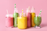 Glasses and bottles of different tasty smoothie with straws on pink background