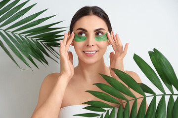 Wall Mural - Pretty young woman with under-eye patches and tropical leaves on light background