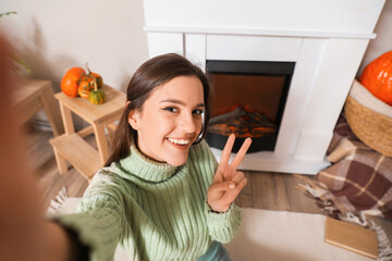 Poster - Young woman taking selfie near fireplace at home, closeup