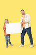© Pixel-Shot - Father and his daughter holding blank poster on yellow background