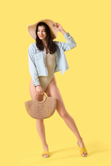 Wall Mural - Beautiful young woman in beachwear with bag on yellow background