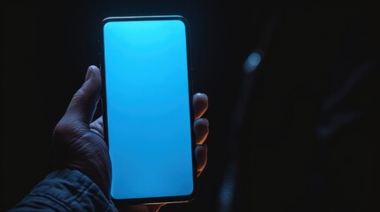 close up young man's hand holding mobile phone with empty screen against neon blue light background,
