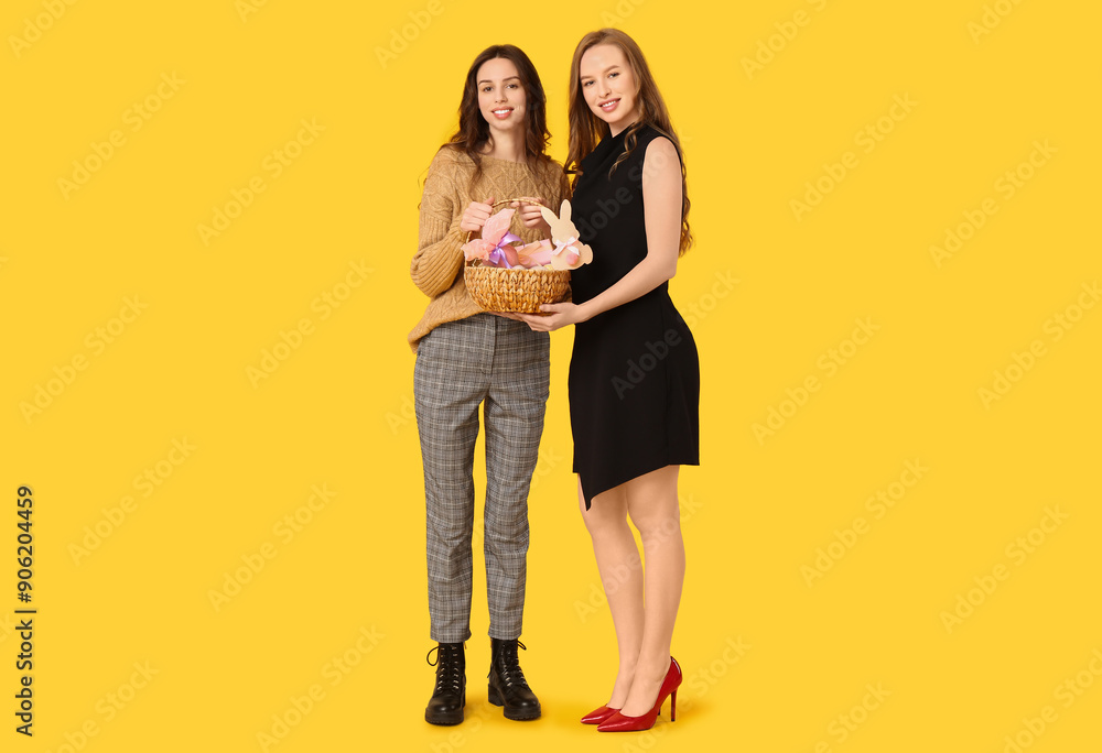 Beautiful young sisters with Easter baskets on yellow background