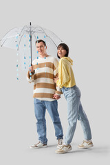 Wall Mural - Young couple holding umbrella with paper drops on light background