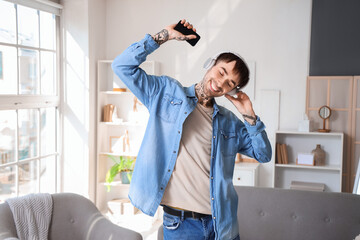 Poster - Young tattooed man in headphones with mobile phone listening to music at home