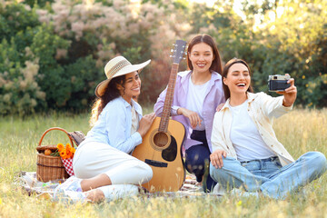 Canvas Print - Female friends with guitar taking selfie on picnic in park