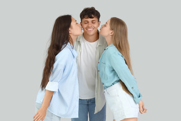 Wall Mural - Young man with two women kissing on light background. Polyamory concept