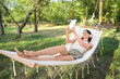 © Pixel-Shot - Young woman with headphones and tablet computer resting in hammock outdoors