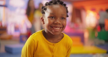 Wall Mural - Portrait of a Little Cute African Girl Looking at the Camera and Smiling. Natural Authentic Portrait of an Innocent Wonderous Black Child with Stylish Hair Playing in Kindergarten