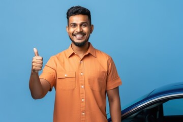 Cheerful man giving thumbs up in front of blue car with blue background