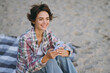 © ViDi Studio - Young smiling fun happy woman wears shirt casual clothes hold in hand use mobile cell phone sit on plaid rest on sea ocean sand shore beach outdoor seaside in summer day free time. Lifestyle concept.