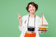 © ViDi Studio - Traveler smiling happy woman wear casual clothes hold ship mockup point finger aside isolated on plain green background. Tourist travel abroad in free spare time rest getaway. Air flight trip concept.