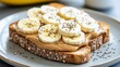 © Atlantist studio - Delicious banana and peanut butter toast topped with chia seeds on a whole grain slice, perfect for a healthy breakfast or snack.