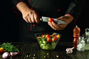 Wall Mural - Preparing a salad with vegetables and cherry tomato. A chef cuts tomatoes for a vegetable menu on a pub kitchen table. Vegetable diet concept