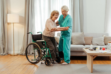 Nurse helping senior woman getting up from wheelchair at home