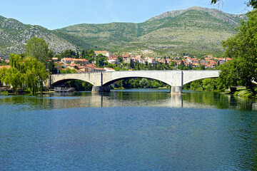 Wall Mural - View towards the Stone Bridge (Kameni most) in Trebinje. Beautiful places in Bosnia and Herzegovina: landscape with the Trebišnjica River, arched bridge, low-rise buildings and mountains