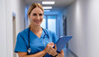 © Matthias - A female nurse with a notepad stands smiling in front of a white hospital corridor.