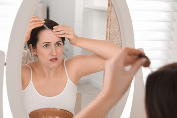 Wall Mural - Hair loss problem. Woman applying serum onto hairline near mirror at home