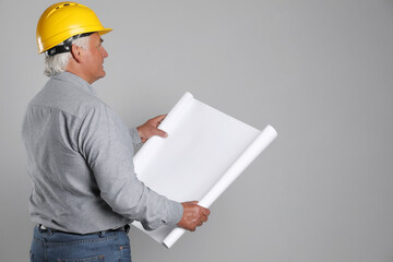 Engineer in hard hat with draft on grey background, space for text