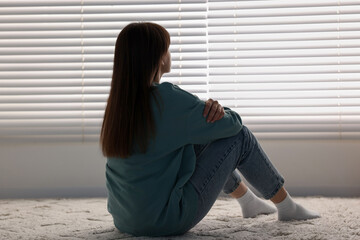 Poster - Loneliness concept. Sad woman sitting on floor at home, back view